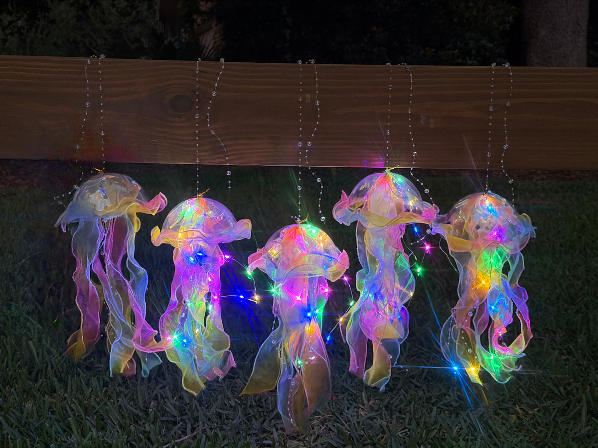 Five tie-dye jellyfish lanterns hanging and illuminated in the dark