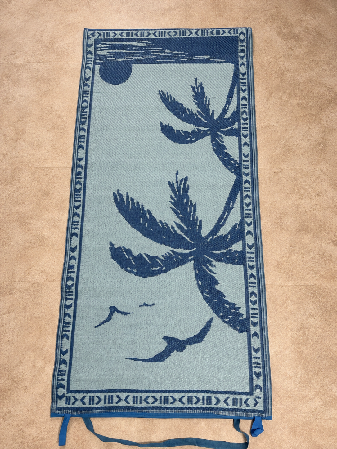 Light blue side of one reversible rug with dark blue palm trees and birds